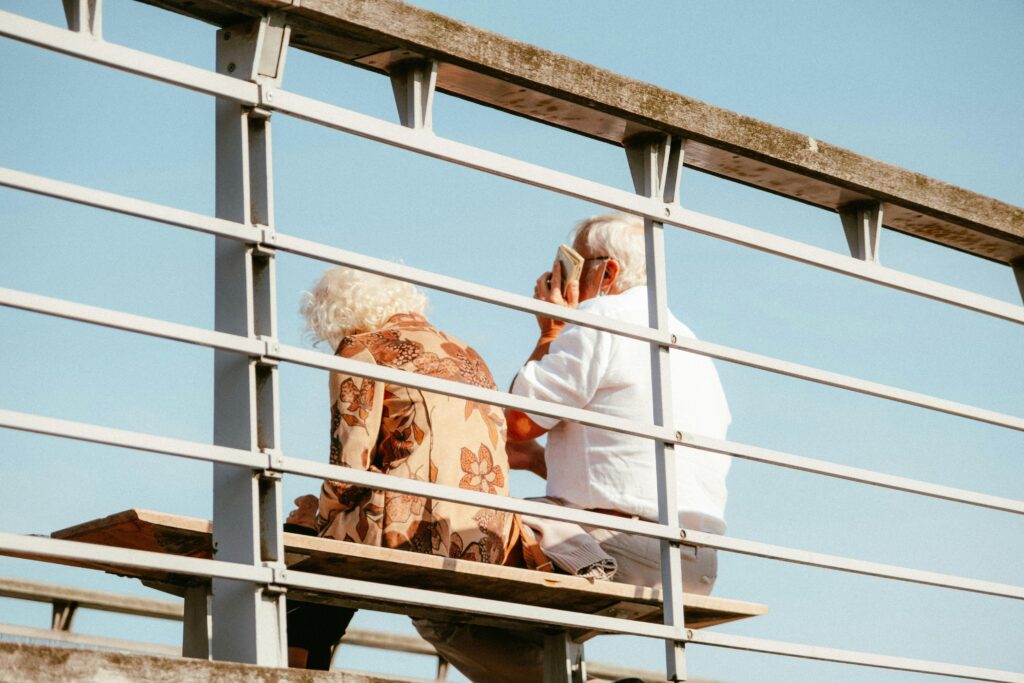 Senior couple sitting on a bench outdoors with blue sky background, enjoying a peaceful moment.